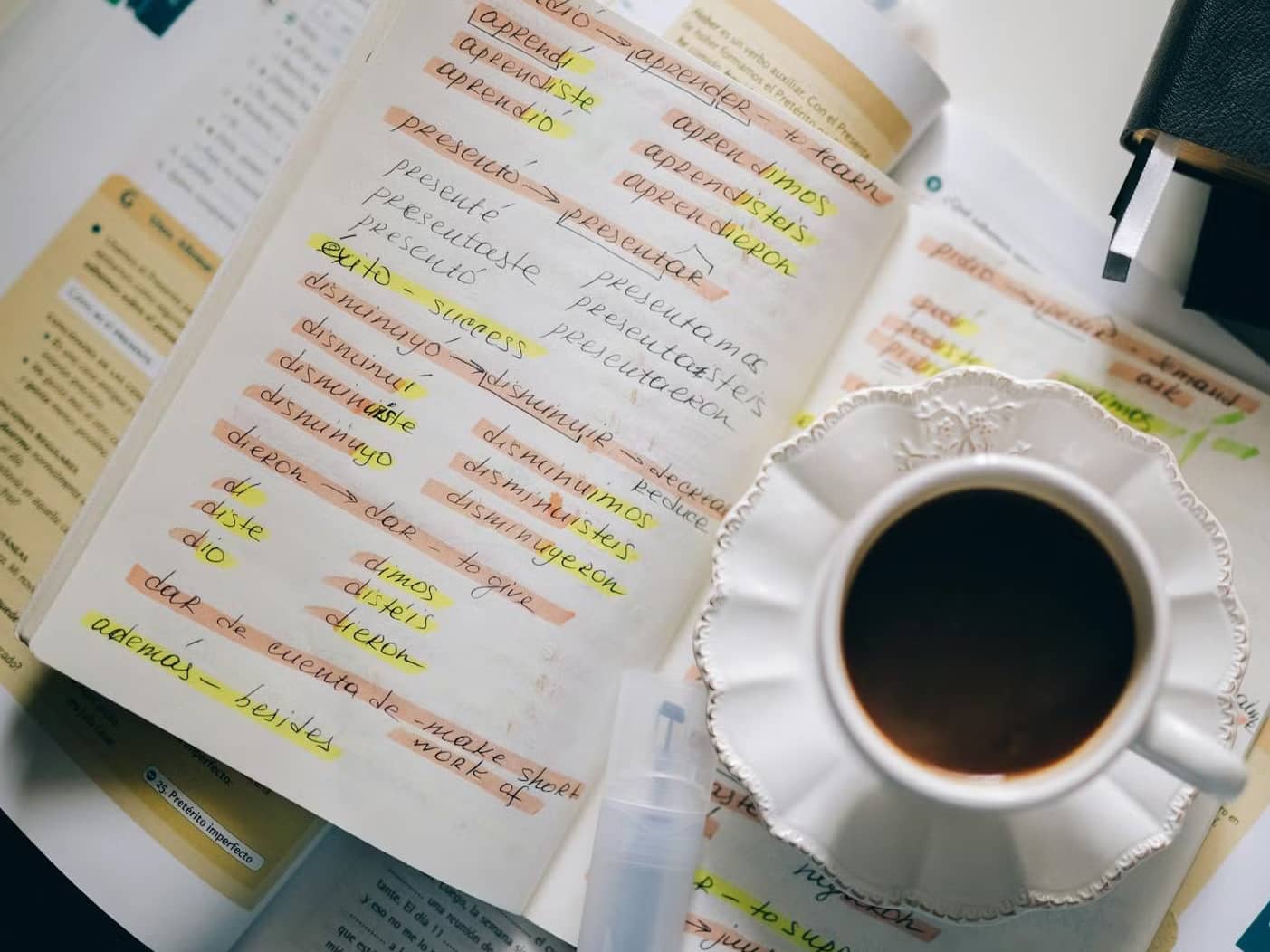 cup of coffee next to notes on spanish words with book.