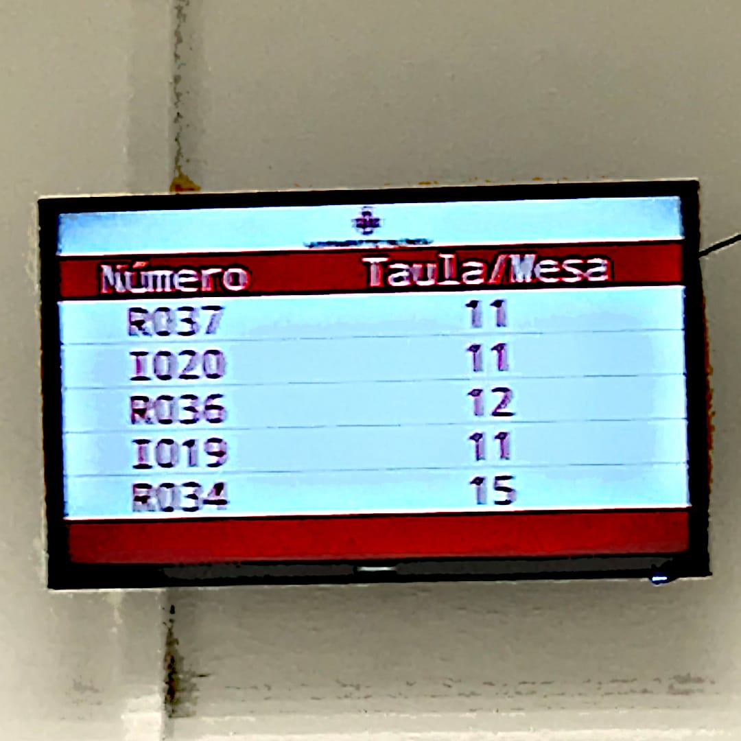 A monitor showing a list of numbers to be called and a corresponding desk to report to.