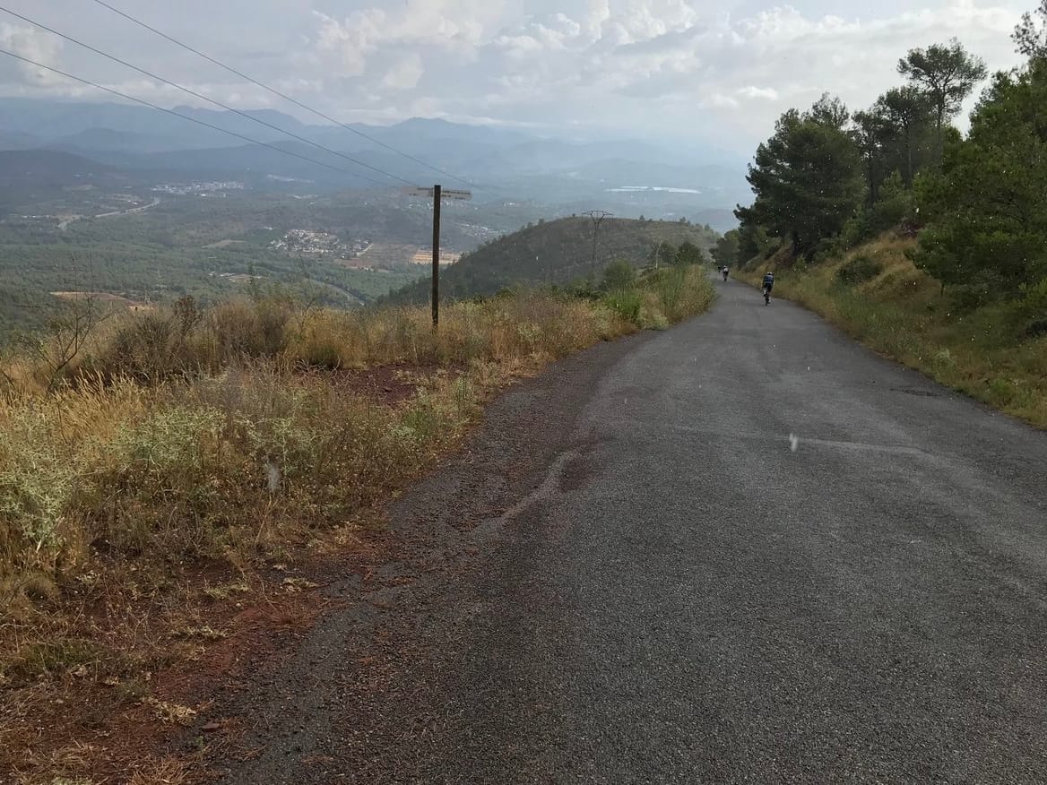 A wet road in the foreground with clouds hovering over the descent to the valley below.
