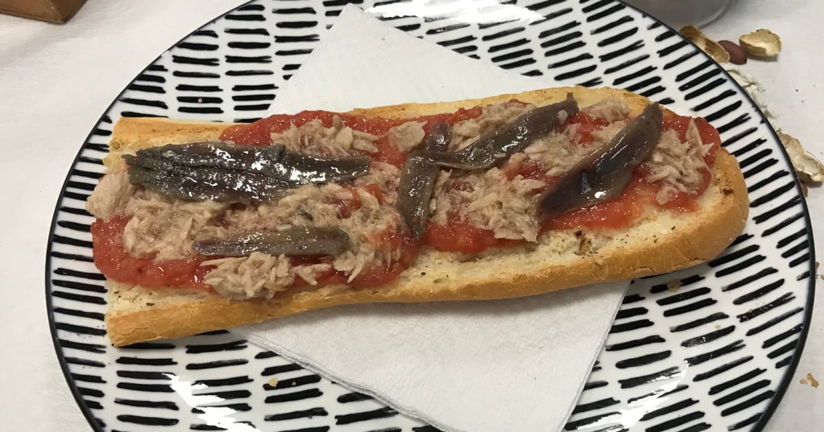 A tostada con tomate y atun, anchoa on a black and white striped plate.