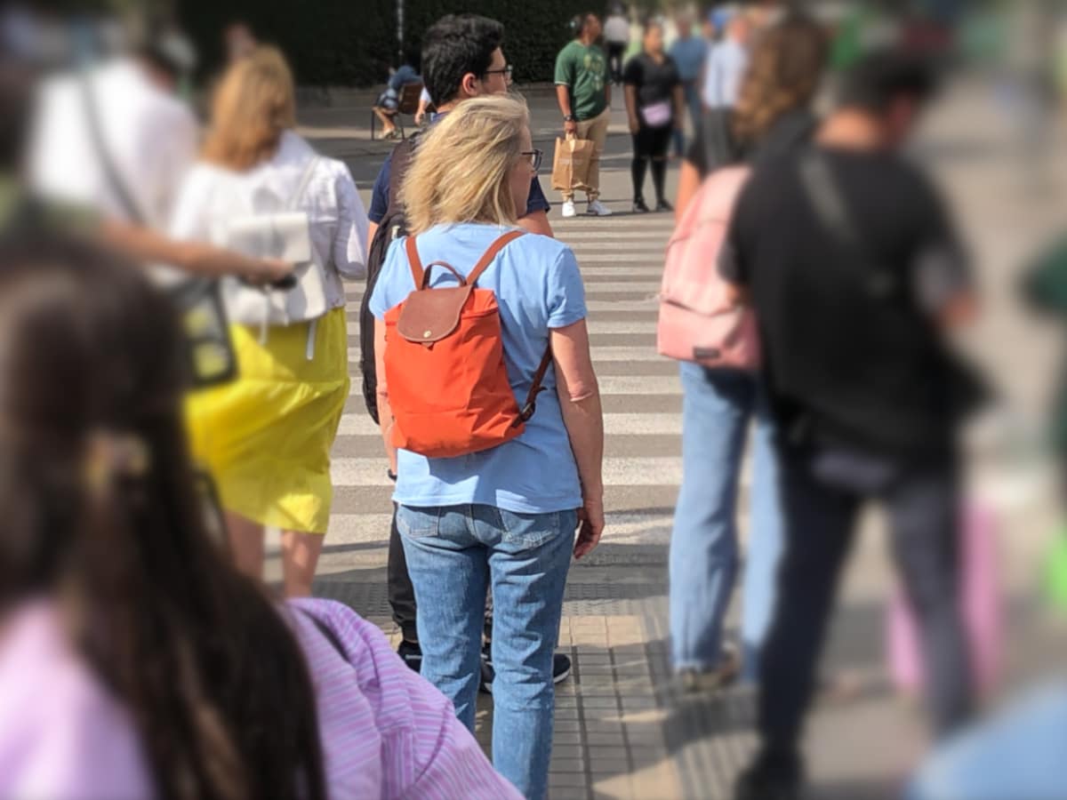 Pedestrians surround a stationary woman wearing an orange backpack.