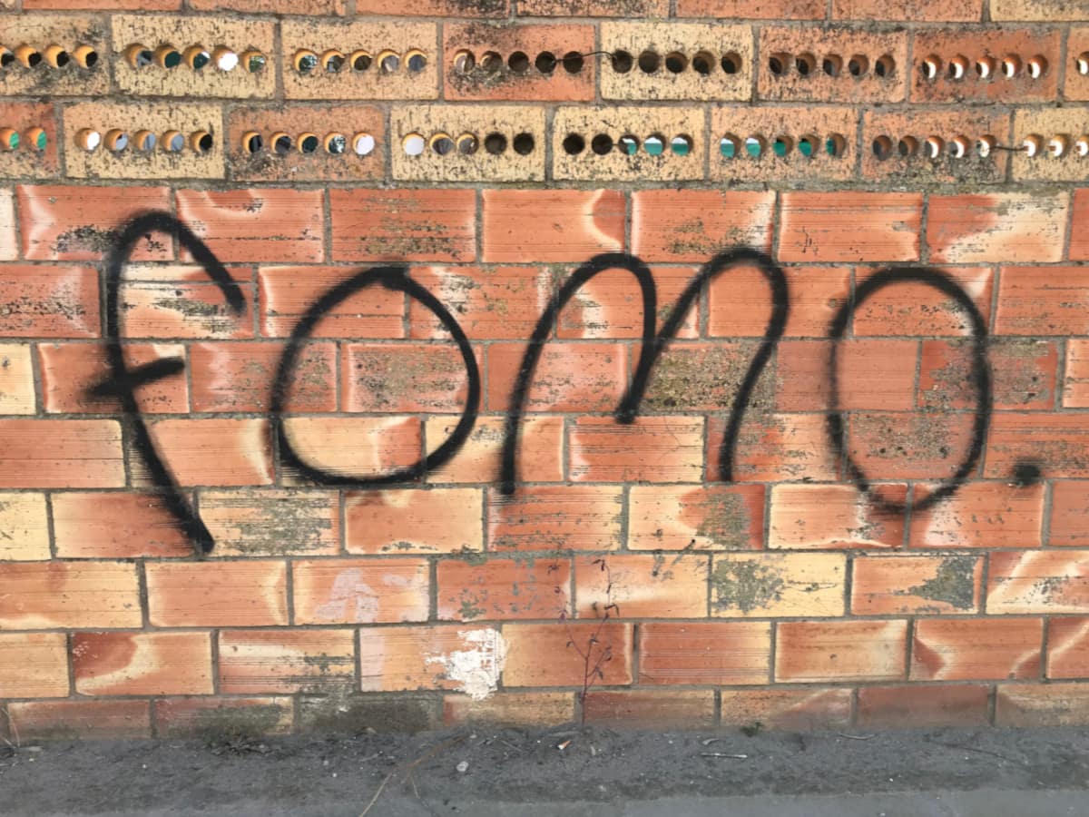 The letters "FOMO" spraypainted on a brick wall.