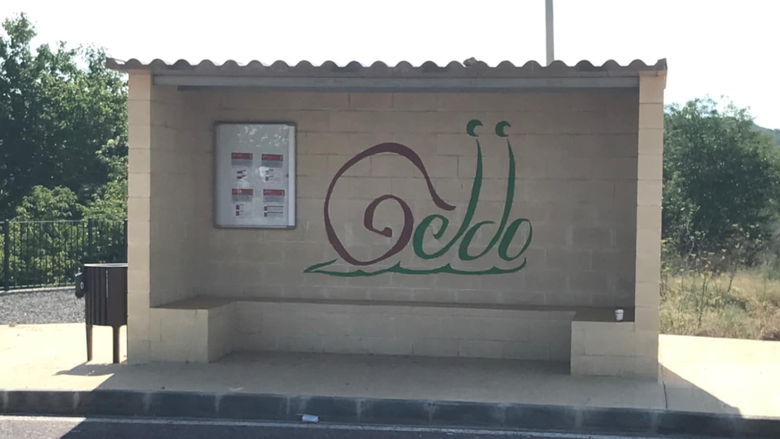 A bus stop with the word "Geldo" painted inside. The word's shape that is of a snail.
