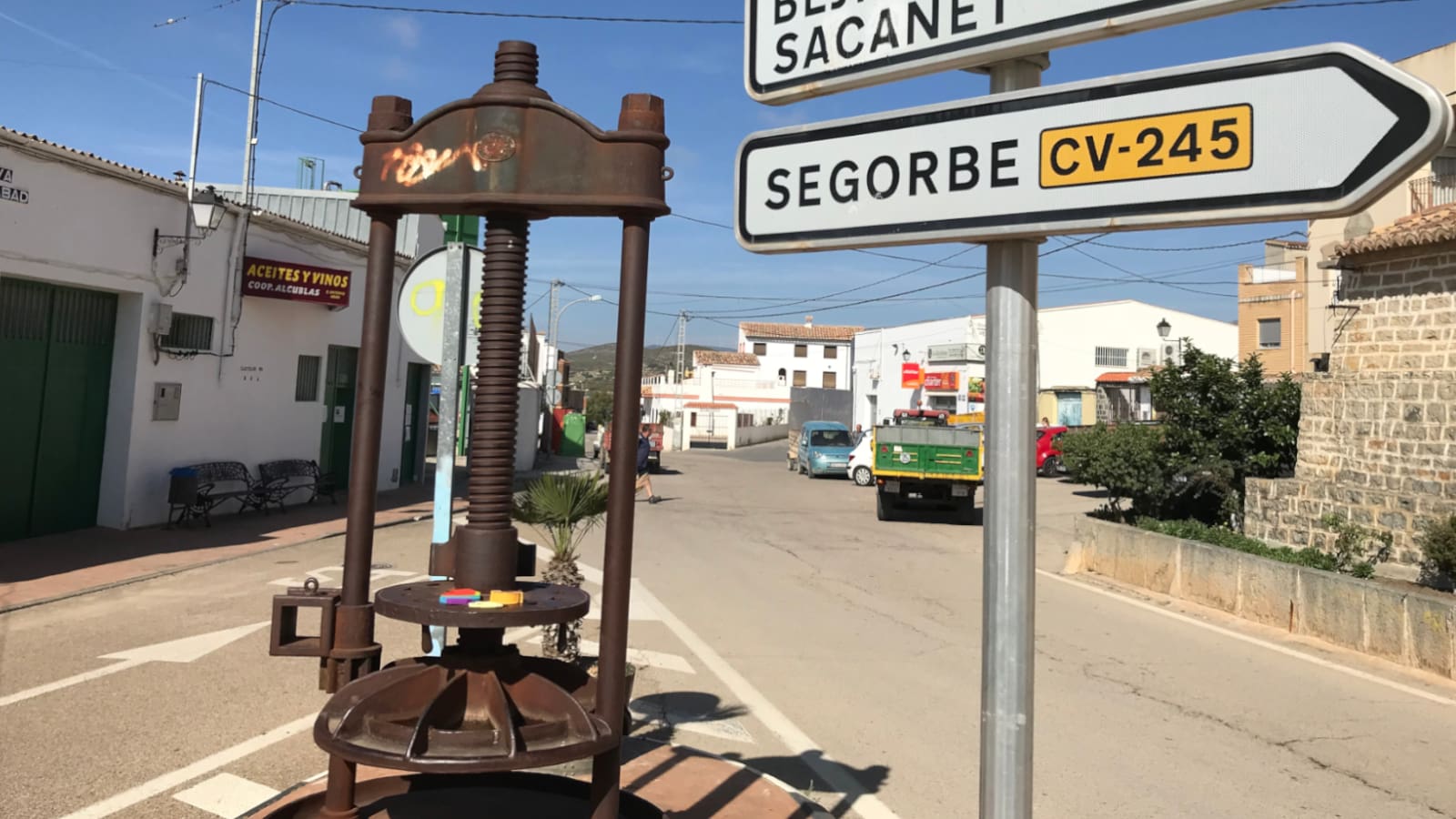 An old machine to press material sits on an intersection's esplanade wtih direction signs