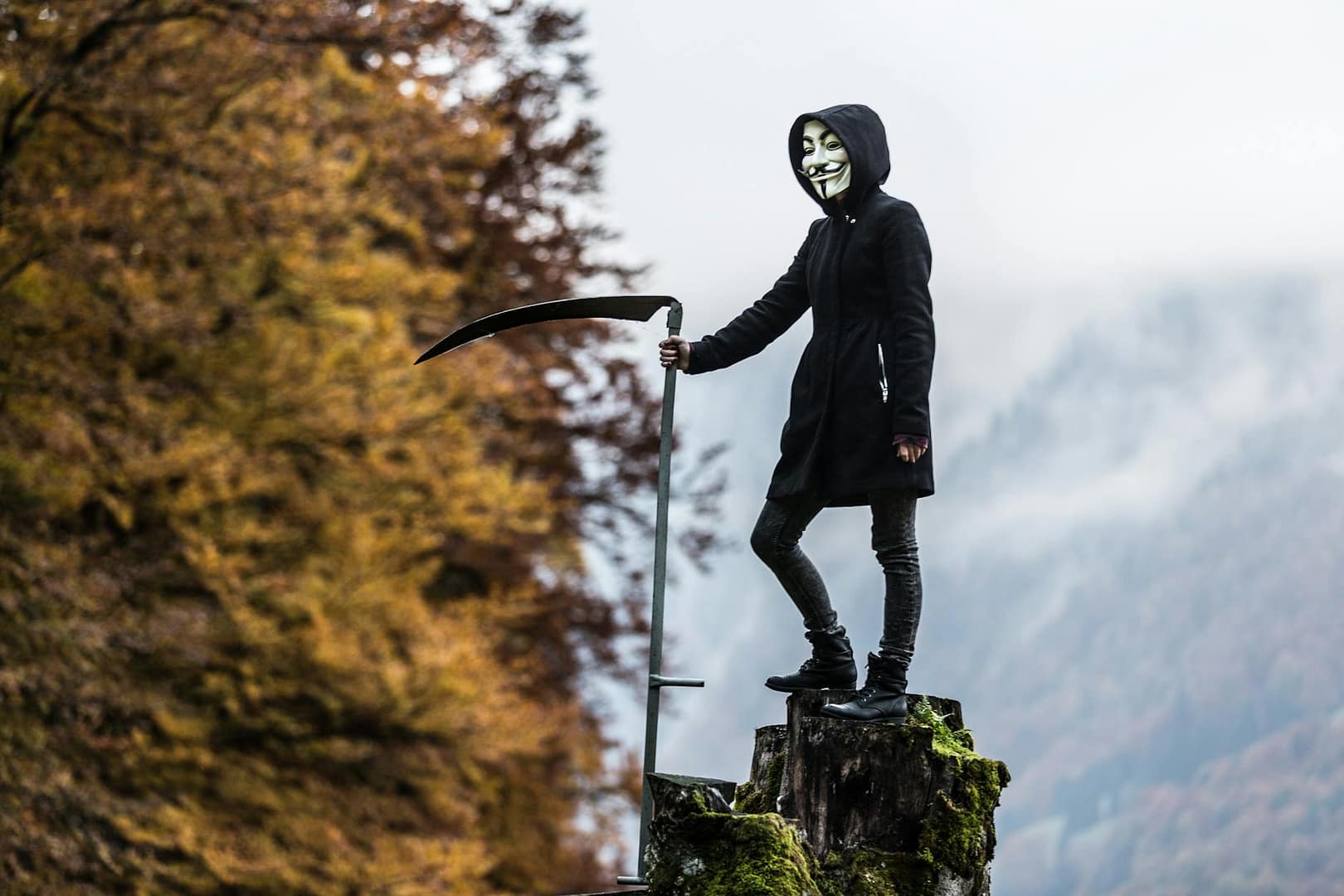 person wearing guy fawkes mask while holding scythe