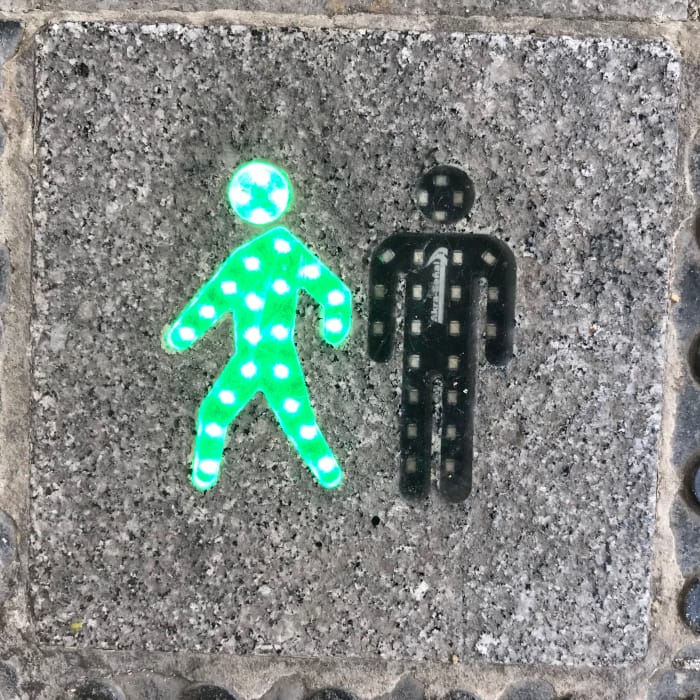 "Walk, Don't Walk" figures on a sidewalk with the the "Walk" figure lit up in green.