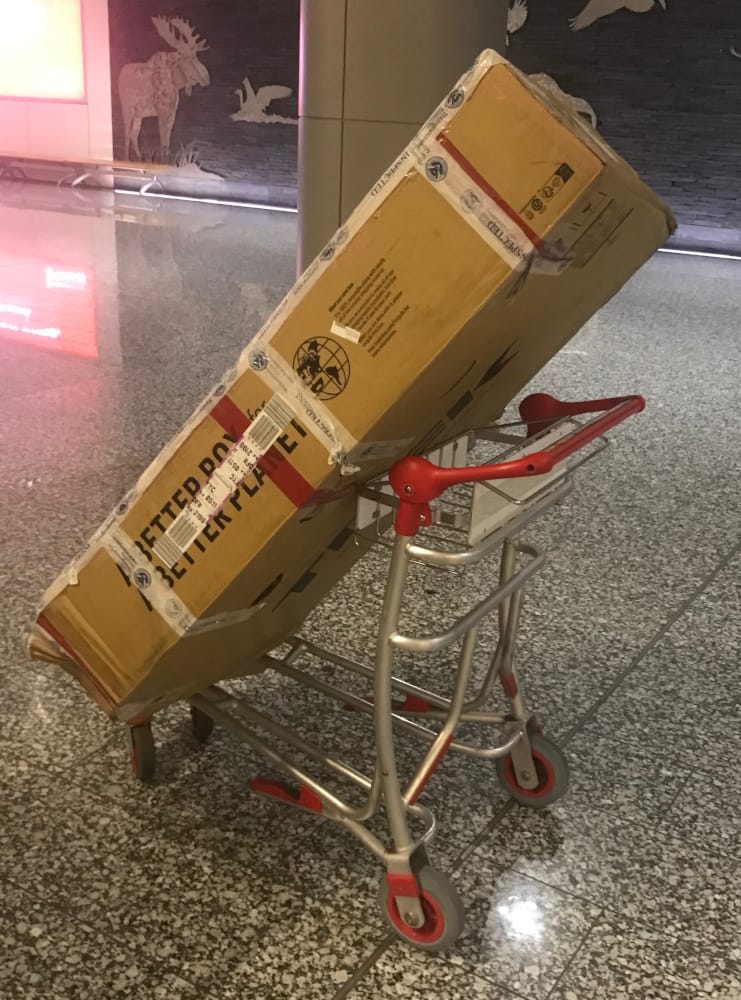 Bike box on its end sitting on an airport pushcart.