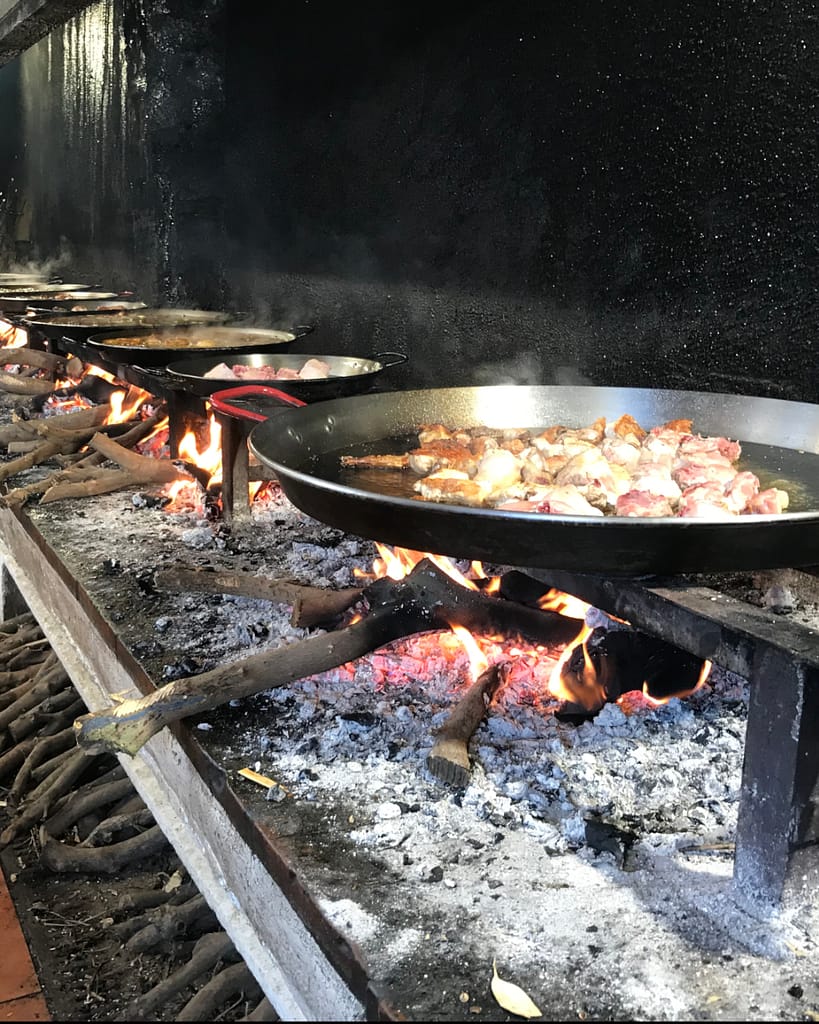 Row of paella pans being heated by a wood-fire stove