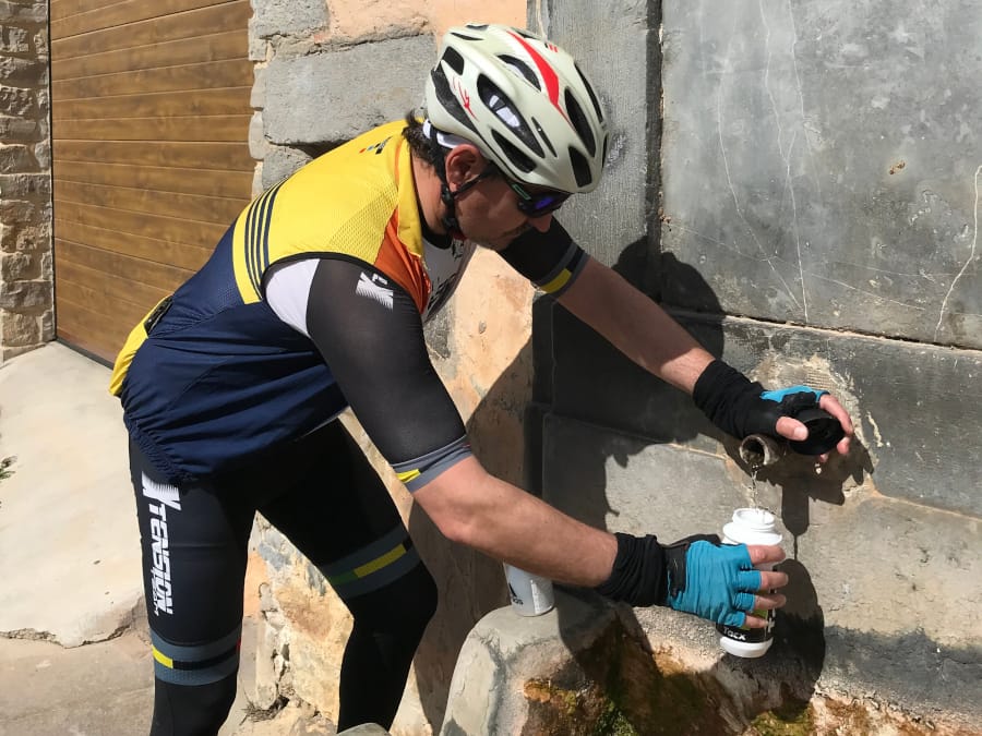 A cyclist in a yellow jersey refills his water bottle at a public fountain.