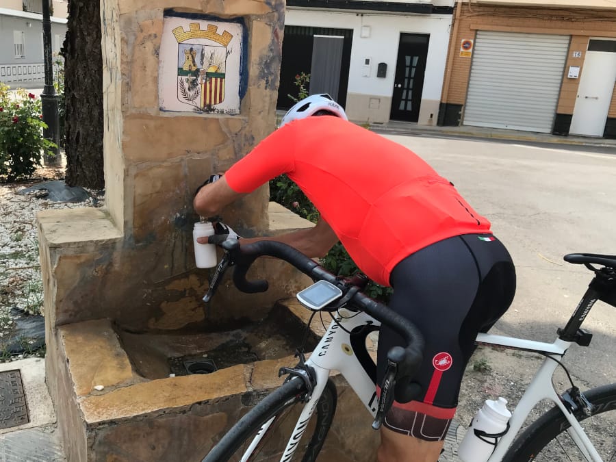 A cyclist in a red jersey refills his water bottle at a public fountain.