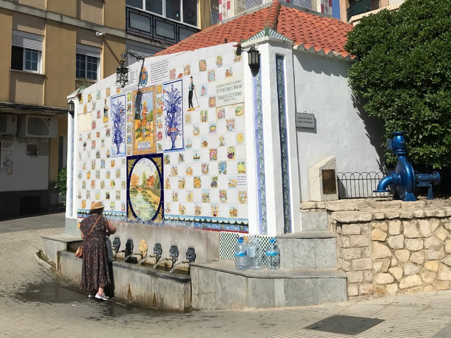 A large, tiled facade over the water pipes as a woman fills her water jugs.