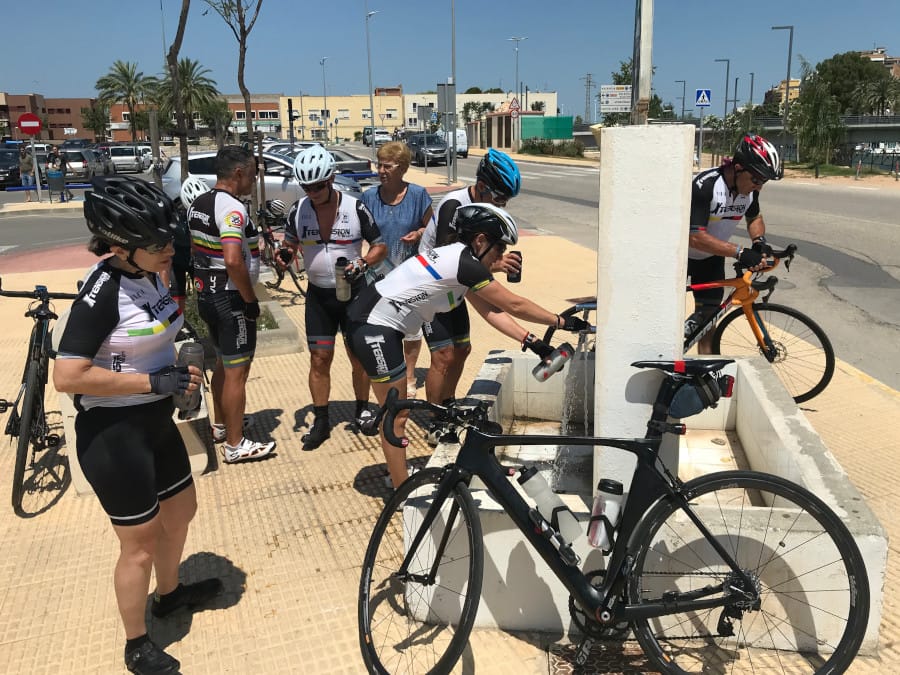A group of cyclists gather around a water fountain to refill their bottles.